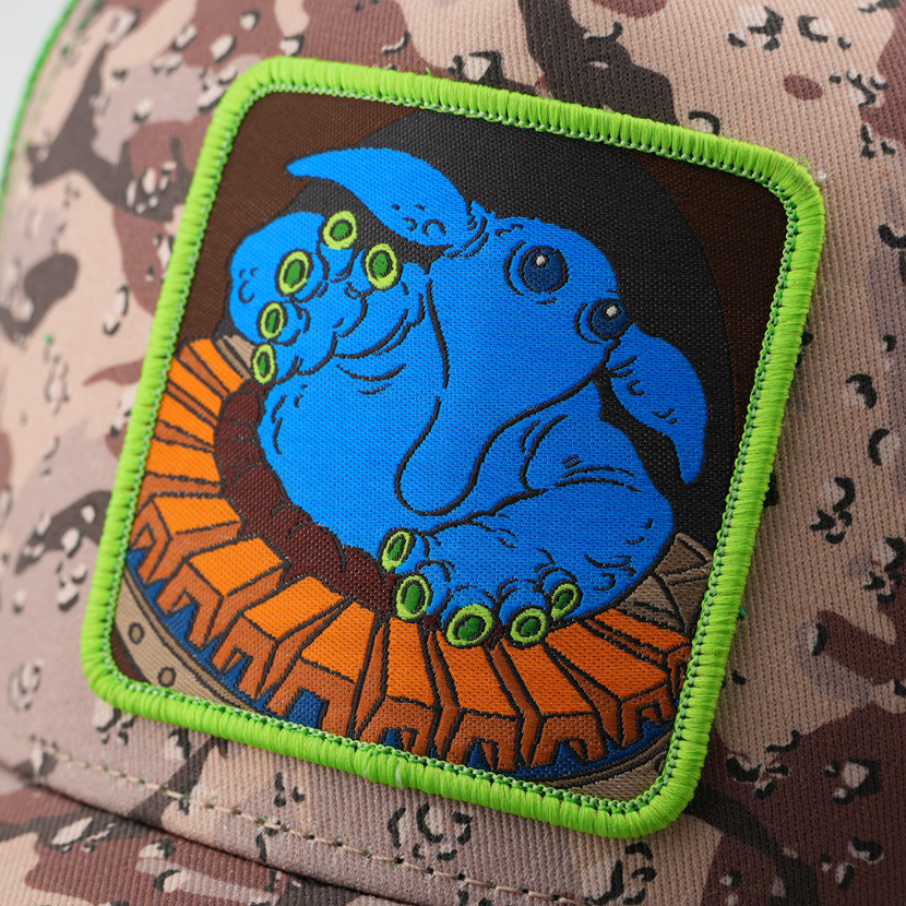 Close-up of a woven Max Rebo from Star Wars patch with a neon green border, stitched onto camo-print trucker cap fabric.