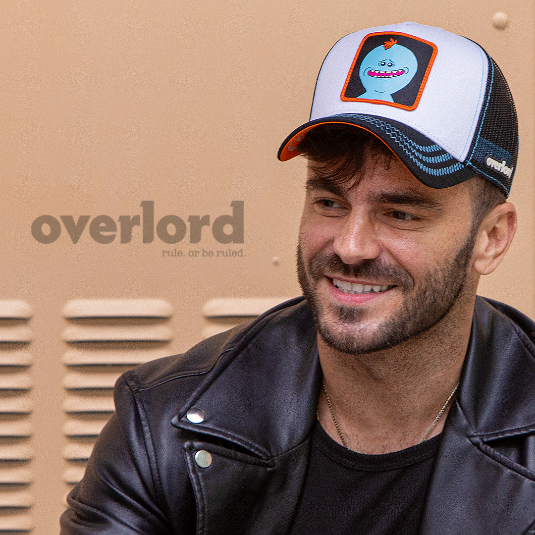 Man wearing white and black OVERLORD X Rick & Morty smiling Meeseeks trucker baseball cap hat with blue zig zag stitching. PVC Overlord logo.