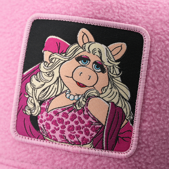 Close-up of a woven patch showing Miss Piggy from The Muppets in a leopard-print top and pearl necklace on a black background, stitched onto fuzzy-textured pink fabric with a pink border.
