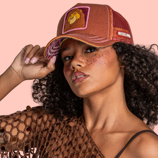 Model wearing the brown Mufasa from Disney's The Lion King retro trucker cap with a patterned brim and dark red mesh side.
