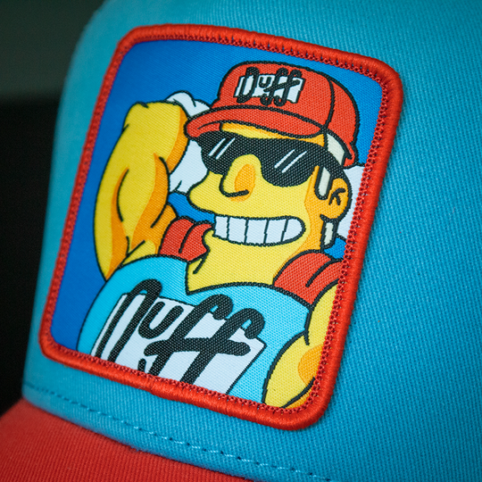 Light Blue and red OVERLORD X The Simpsons present smiling Duffman trucker baseball cap hat woven Overlord patch closeup.