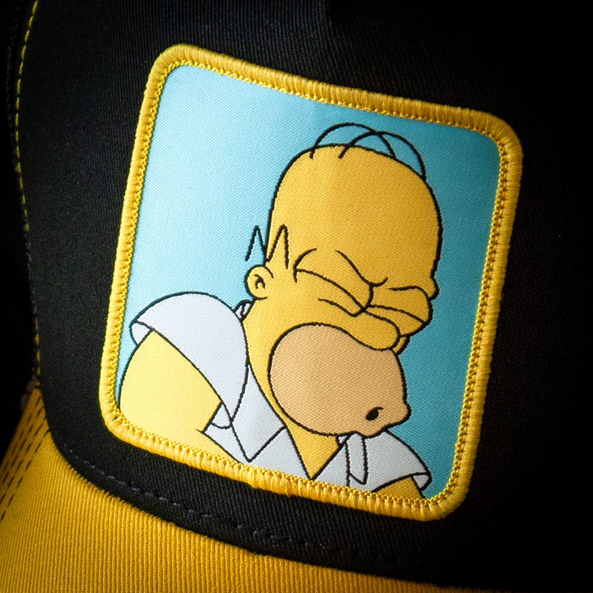 Black and yellow OVERLORD X The Simpsons Homer Doh trucker baseball cap hat woven Overlord patch closeup.