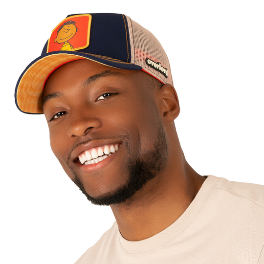 Man wearing navy blue twill trucker cap with khaki mesh featuring a woven patch of Franklin from the Peanuts Comics attached to the crown.