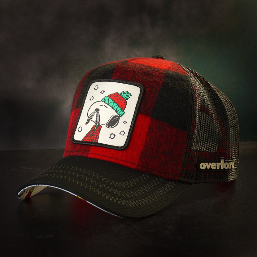 Red and black buffalo plaid flannel trucker cap with black mesh featuring a woven patch of Lumberjack Snoopy from the Peanuts attached to the crown.