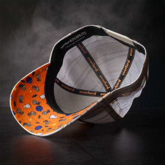 Inside view of cream colored trucker cap with printed Peanuts Halloween icons printed on orange underbrim.