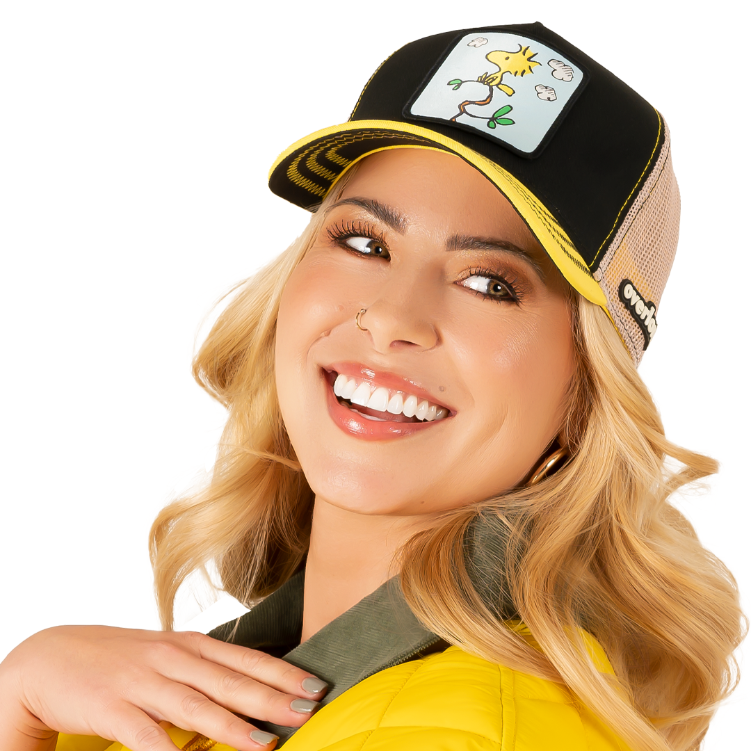 Woman wearing black and yellow twill trucker cap with khaki mesh featuring a woven patch of Woodstock from Peanuts on the crown.