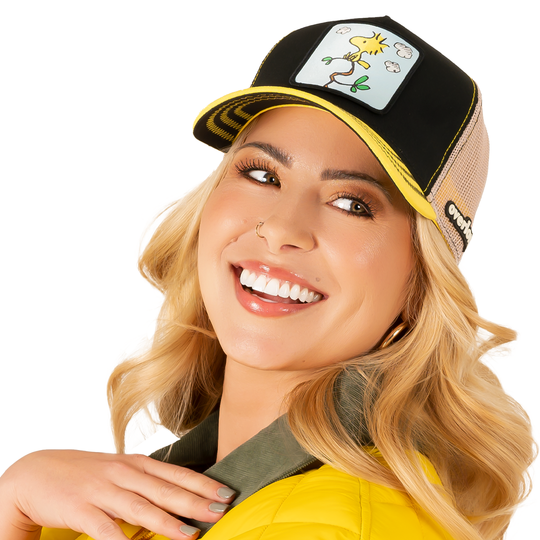 Woman wearing black and yellow twill trucker cap with khaki mesh featuring a woven patch of Woodstock from Peanuts on the crown.