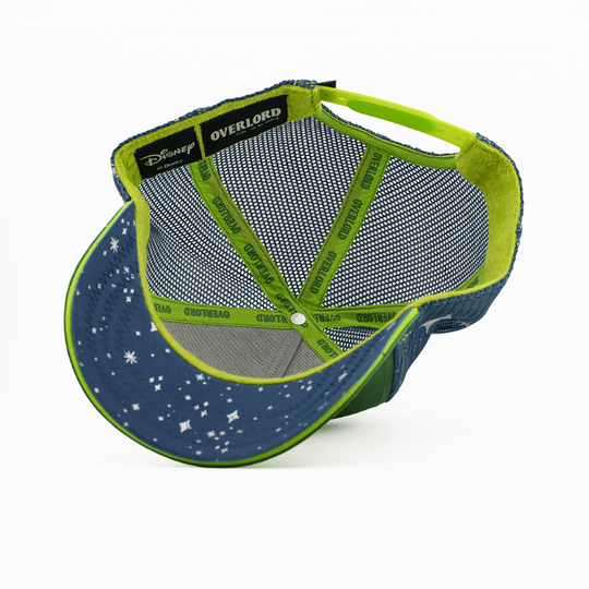 Underside of the Peter Pan from Disney's Peter Pan retro trucker cap showing a navy starry-print brim, a Disney tag, navy mesh crown, and green Overlord branded taping.
