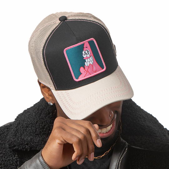 Man wearing black and tan OVERLORD X SpongeBob Big Smile Patrick trucker baseball cap hat with pink zig zag stitching. PVC Overlord logo.