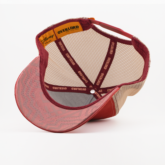 Underside of the Pumbaa from Disney's The Lion King retro trucker cap showing a pink patterned brim, tan mesh crown, Disney tag, and dark red Overlord branded taping with tan text.