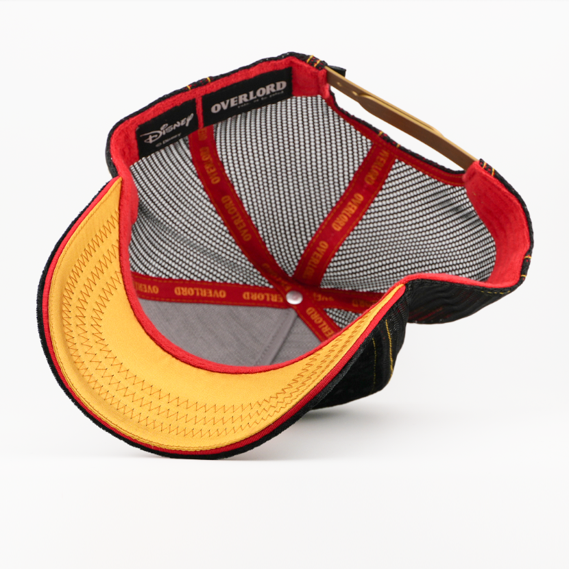 Underside of the Evil Queen retro trucker cap showing a gold brim, Disney tag, black mesh crown, and red Overlord taping.