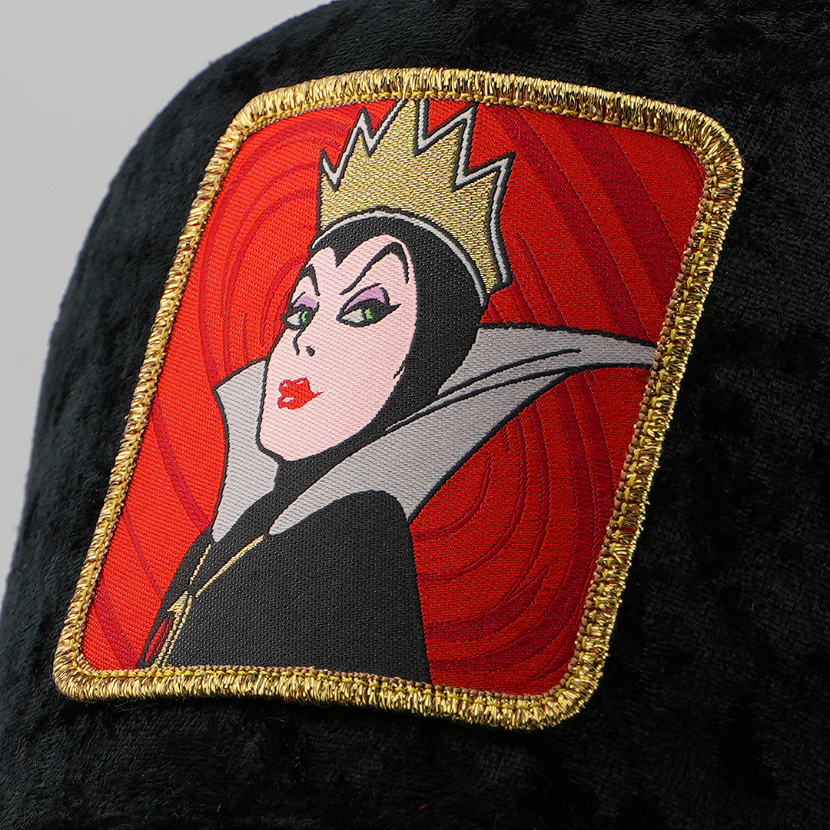 Close-up of the Evil Queen from Disney's Snow White and the Seven Dwarfs patch against a swirling red background, stitched onto the black velvet retro trucker cap fabric with gold border.