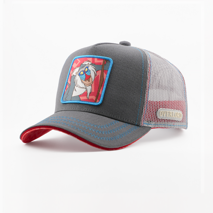 Grey corduroy-textured retro trucker cap with a woven Rafiki from Disney's The Lion King patch on a red patterned background with a blue border, red-trimmed brim, grey mesh back with Overlord logo.