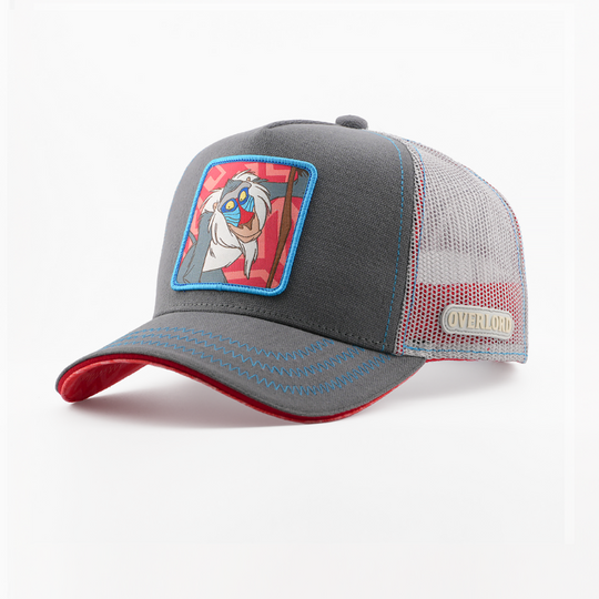 Grey corduroy-textured retro trucker cap with a woven Rafiki from Disney's The Lion King patch on a red patterned background with a blue border, red-trimmed brim, grey mesh back with Overlord logo.