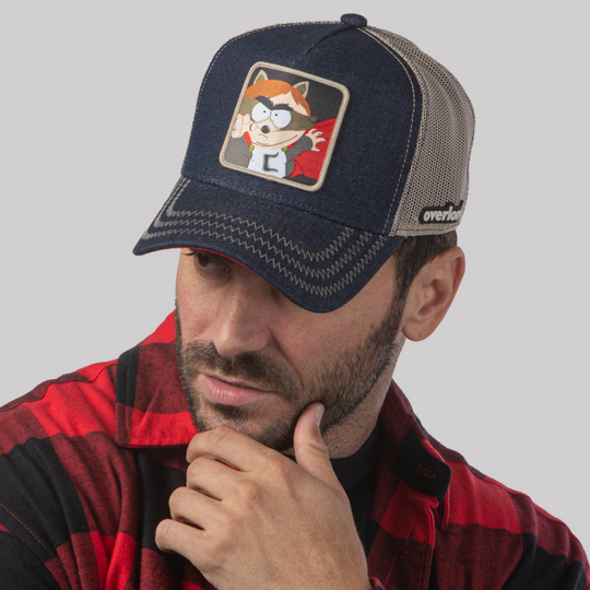 Man wearing dark blue denim OVERLORD X South Park Cartman Coon trucker baseball cap hat with khaki zig zag stitching. PVC Overlord logo.
