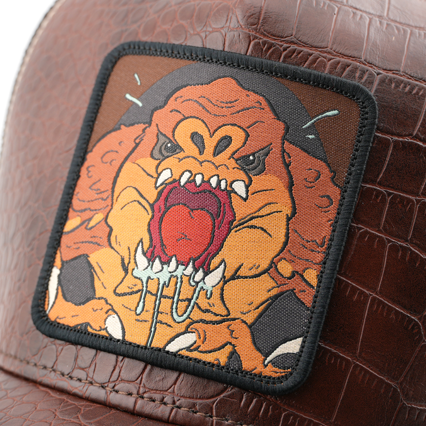 Close-up of a woven roaring Rancor from Star Wars patch, stitched onto brown croc-print trucker cap fabric.