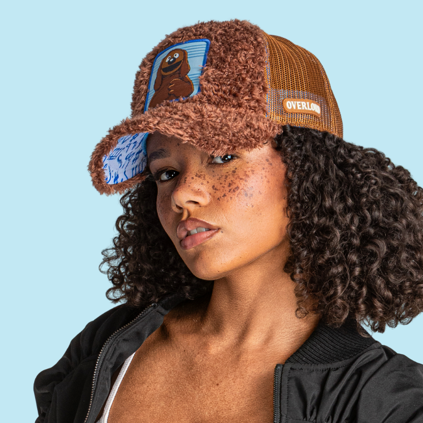 Model wearing the fuzzy-textured brown Rowlf the Dog from The Muppets retro trucker cap with a light blue printed brim and brown mesh side.