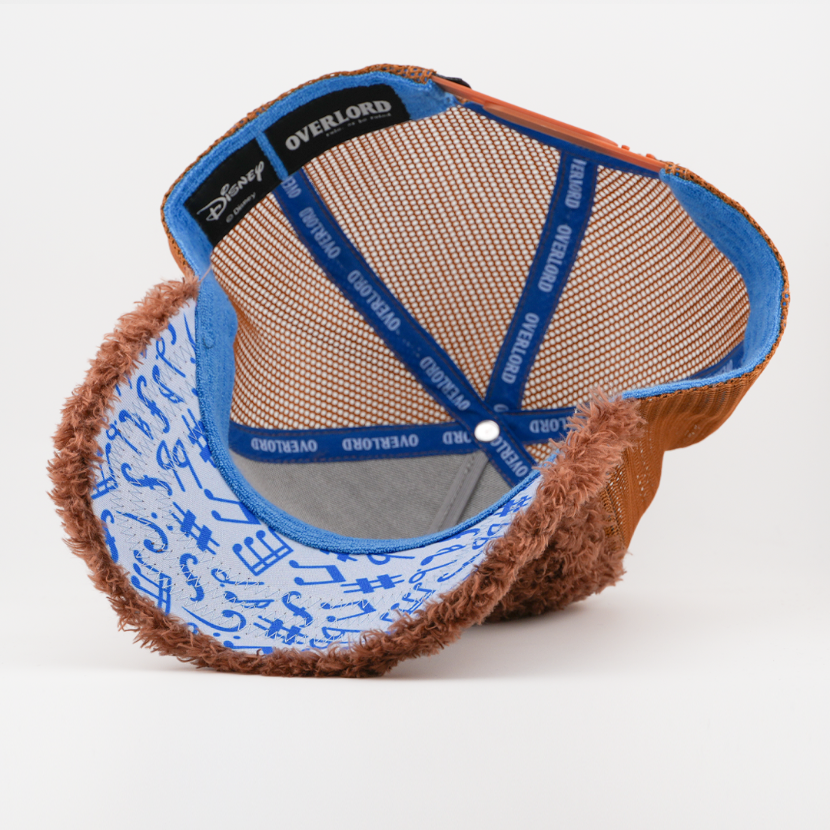 Underside of the Rowlf the Dog retro trucker cap, showing a musical-note print brim, a Disney tag, brown mesh crown, and blue Overlord branded taping with white text.