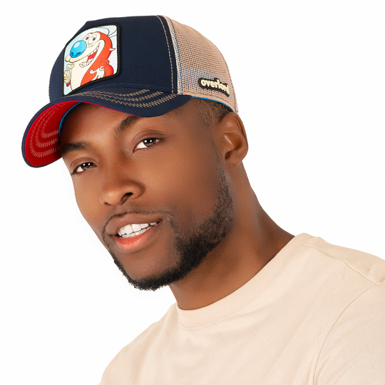 Man wearing navy OVERLORD X Ren and Stimpy smiling Stimpy trucker baseball cap hat with khaki zig zag stitching. PVC Overlord logo.