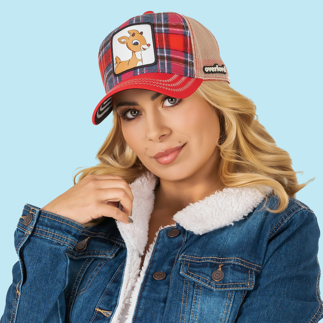 Woman wearing red and blue plaid trucker cap with khaki mesh featuring a woven patch of Rudolph the Red Nose Reindeer on the crown.