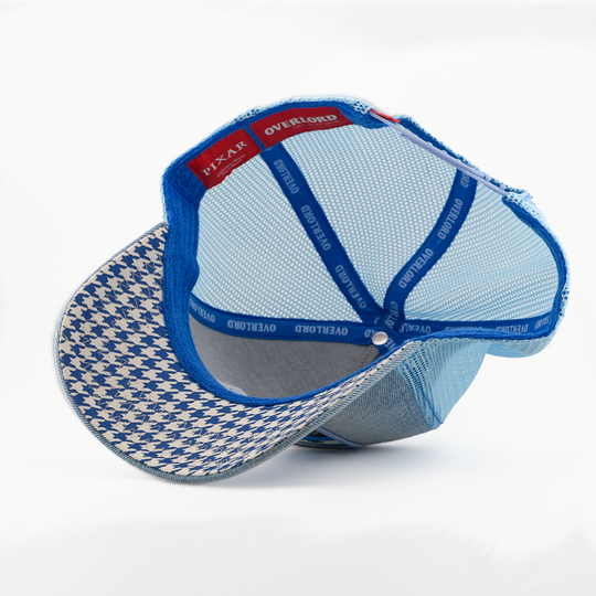 A light blue mesh trucker-style cap shown from the back, featuring a blue and white houndstooth patterned visor, blue elastic back straps, and a red interior label.
