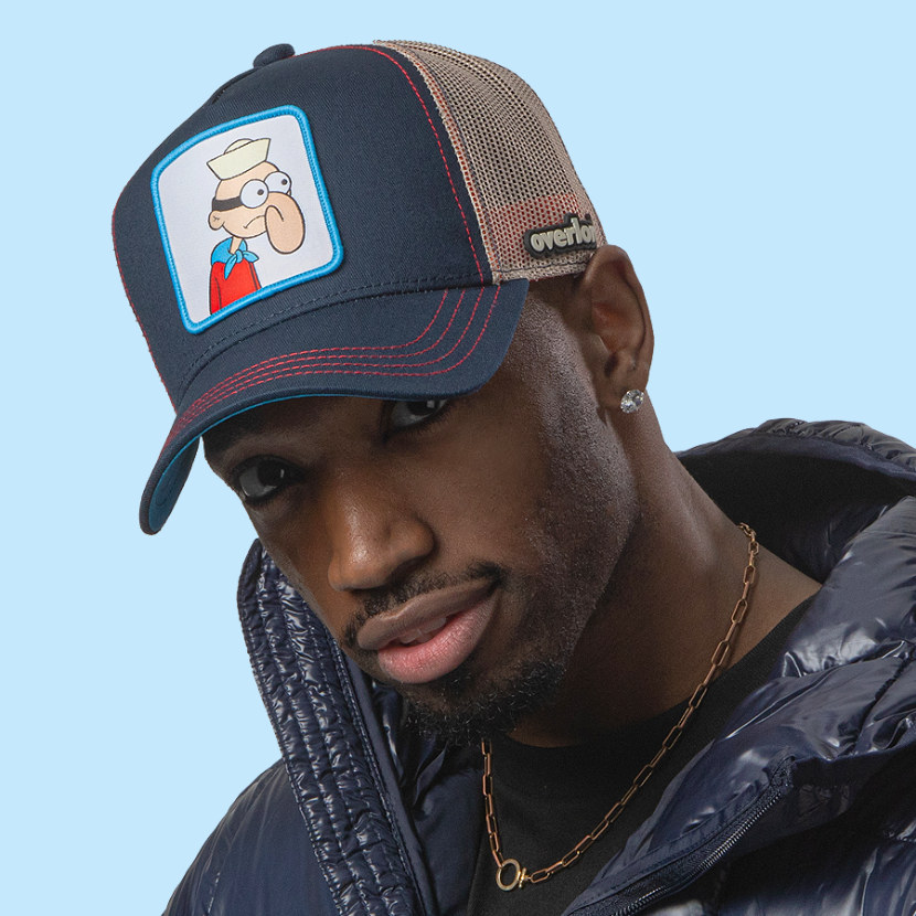 Man wearing navy OVERLORD X SpongeBob Barnacle Boy trucker baseball cap hat with red stitching. PVC Overlord logo.