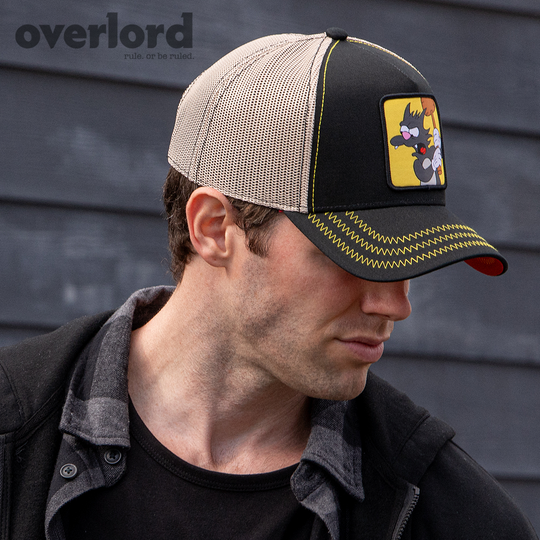 Man wearing black OVERLORD X The Simpsons Scratchy the cat trucker baseball cap hat with yellow zig zag stitching. PVC Overlord logo.