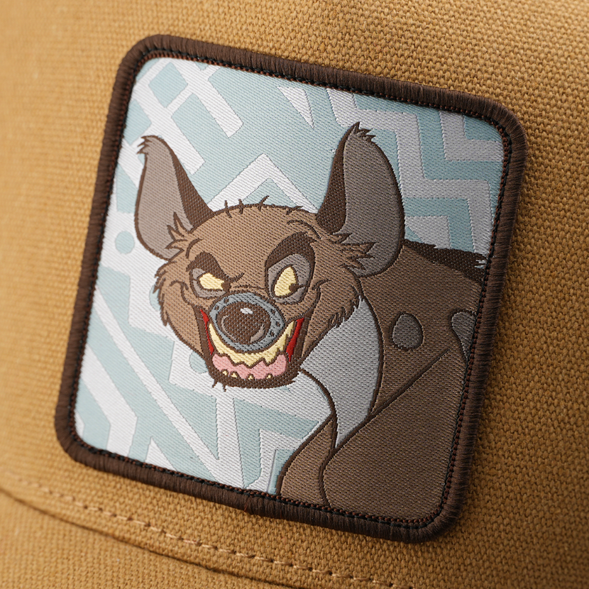 Close-up woven patch of Banzai from Disney's The Lion King snarling, on a light blue patterned background with a brown border, stitched onto a tan corduroy-textured retro trucker cap.