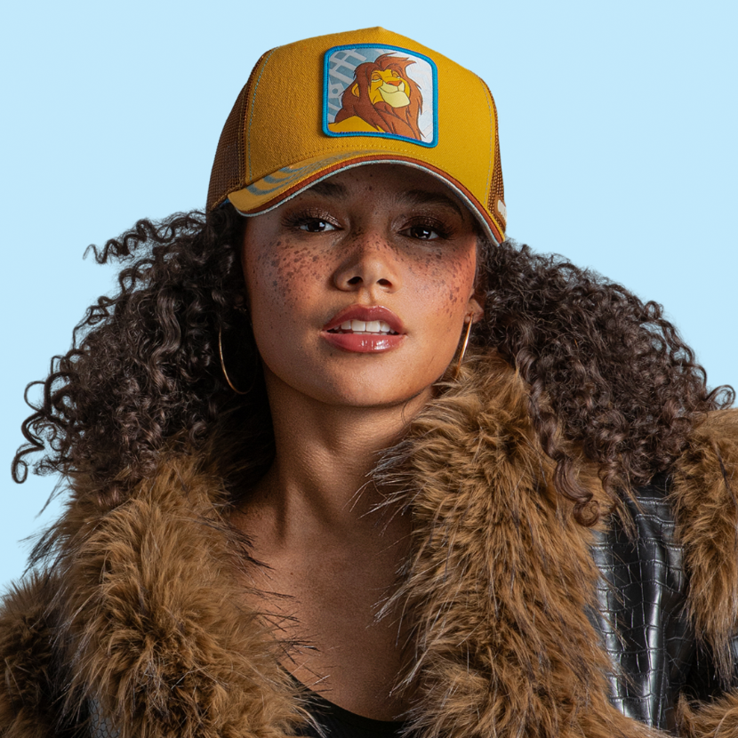 Close-up woven patch of adult Simba from Disney's The Lion King with eyes closed in contentment, on a light blue patterned background with a blue border, stitched onto a yellow corduroy-textured retro trucker cap.