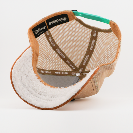 Underside of the Sleepy from Disney's Snow White and the Seven Dwarfs retro trucker cap showing a white fuzzy-textured brim, a Disney tag, tan mesh crown, and brown Overlord branded taping.