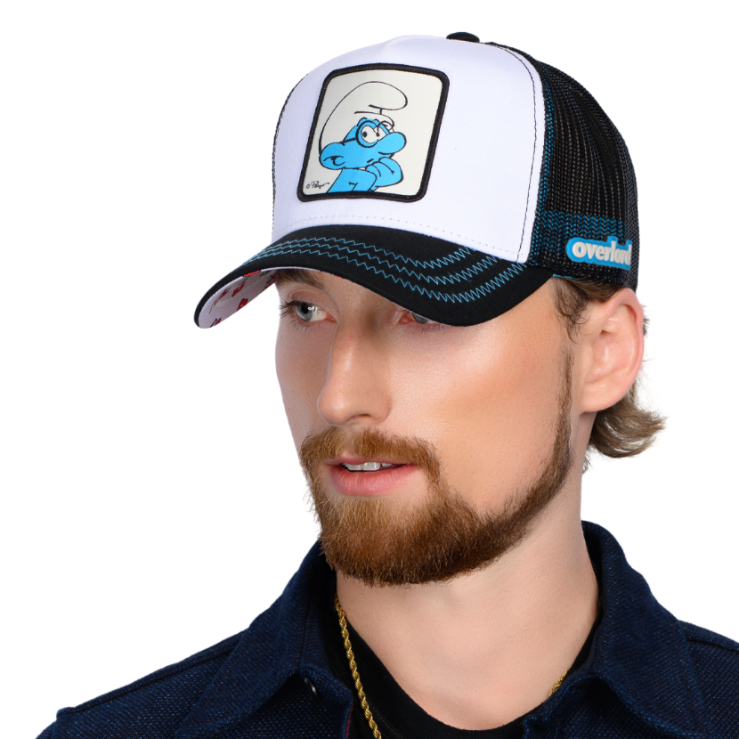 Man wearing black and white twill trucker cap with black mesh featuring a woven patch of Brainy Smurf from the Smurfs attached to crown
