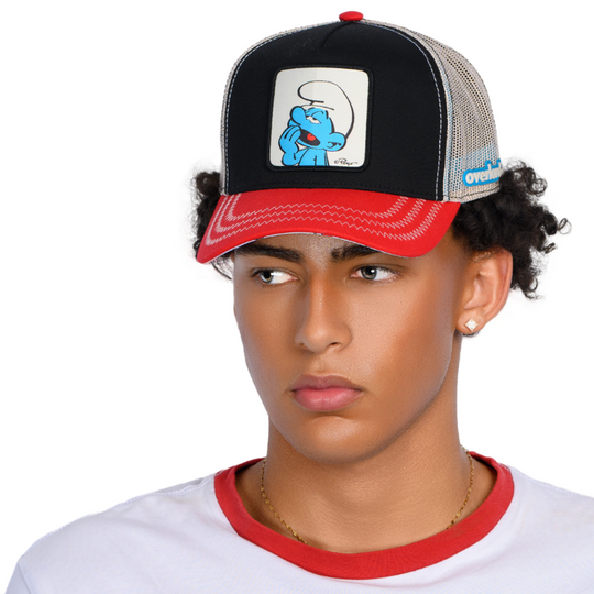 Man wearing black and red twill trucker cap with cream mesh featuring a woven patch with Lazy Smurf from the Smurfs attached to crown