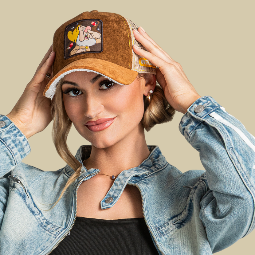 Model wearing the brown suede-textured Sneezy from Disney's Snow White and the Seven Dwarfs retro trucker cap with a brown brim and mesh side.