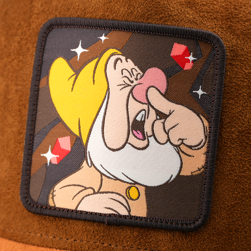 Woven patch of Sneezy from Disney's Snow White and the Seven Dwarfs mid-sneeze against a gem and mine-themed background, with a black border, stitched onto the brown suede-textured retro trucker cap.