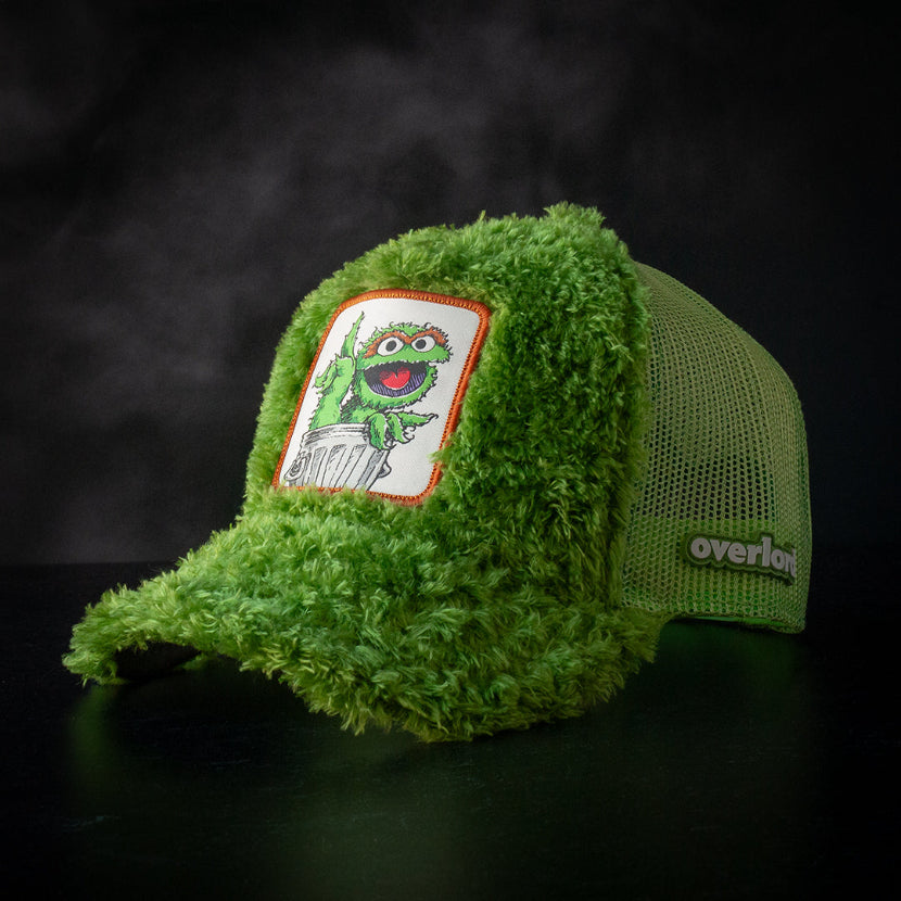 Green faux fur trucker cap hat featuring Oscar the Grouch from Sesame Street on woven patch attached to crown against black background