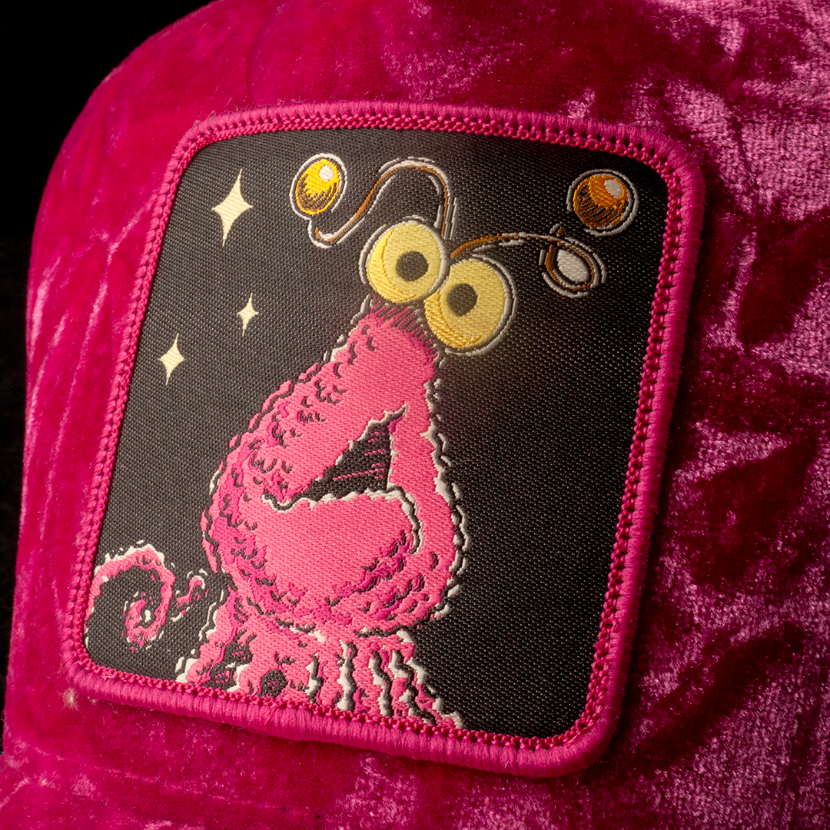 Close-up of Sesame Street pink yip martian woven patch on hot pink crushed velvet trucker cap hat