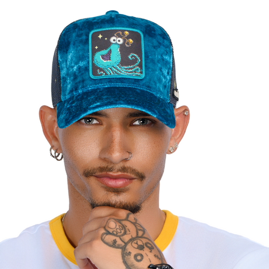 Man wearing blue crushed velvet trucker cap hat with Sesame Street blue yip martian woven patch against white background