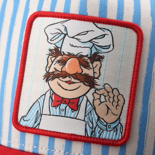 Close-up of a woven patch showing the Swedish Chef from The Muppets with a chef's hat and red bow tie giving an OK sign, stitched onto blue and white striped fabric with a red border.