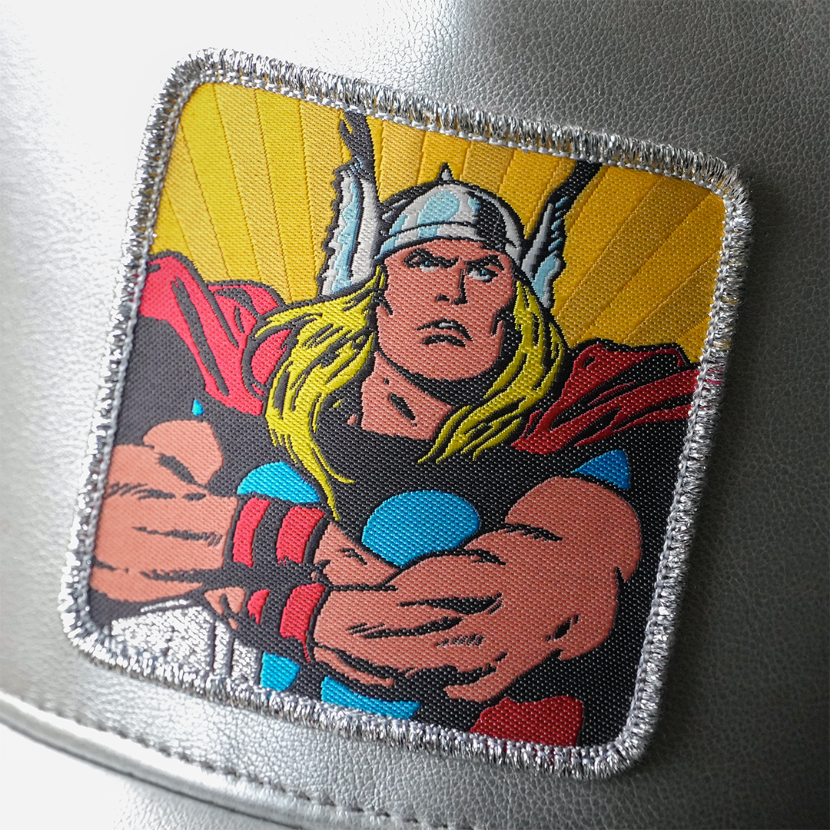 Close-up of a woven Marvel's Thor patch with arms crossed, stitched onto metallic silver cap fabric.