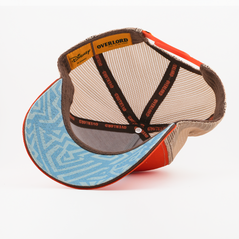 Underside of the Timon from Disney's The Lion King retro trucker cap showing a blue patterned brim with orange trim, tan mesh crown, Disney tag, and brown Overlord branded taping with orange text.