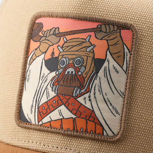 Close-up of a woven Tusken Raider from Star Wars patch wielding a gaderffii stick, stitched onto tan canvas cap fabric.