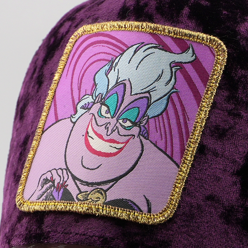 Close-up of the Ursula from Disney's The Little Mermaid patch with a swirling pink background, stitched onto the purple velvet retro trucker cap fabric.