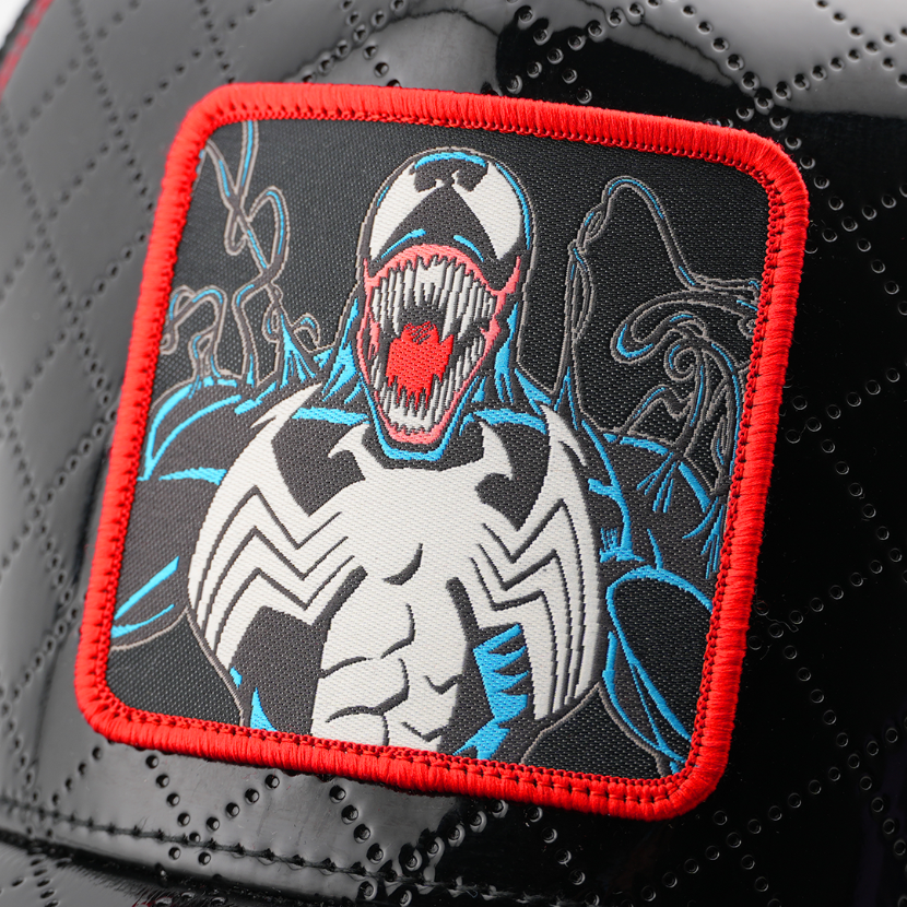 Close-up of a woven Marvel's Venom patch with a red border, stitched onto glossy black quilted cap fabric.