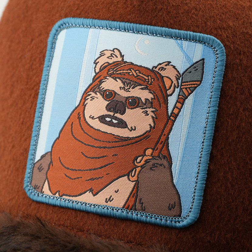 Close-up of a woven Wicket the Ewok from Star Wars patch holding a spear, stitched onto brown wool-look cap fabric.