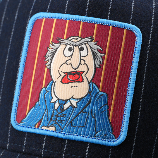 Close-up of a woven patch showing Waldorf from The Muppets in a blue pinstriped suit with an open mouth on a red striped background, stitched onto navy pinstriped fabric with a light blue border.