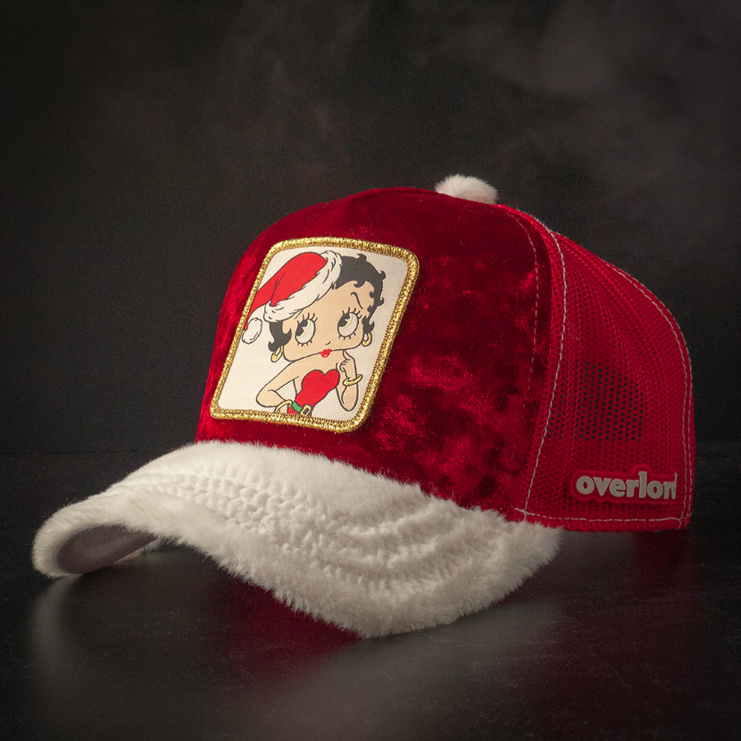 Red crushed velvet trucker cap with white faux fur brim and red mesh featuring a woven patch of Betty Boop wearing a Santa hat and red dress attached to the crown.