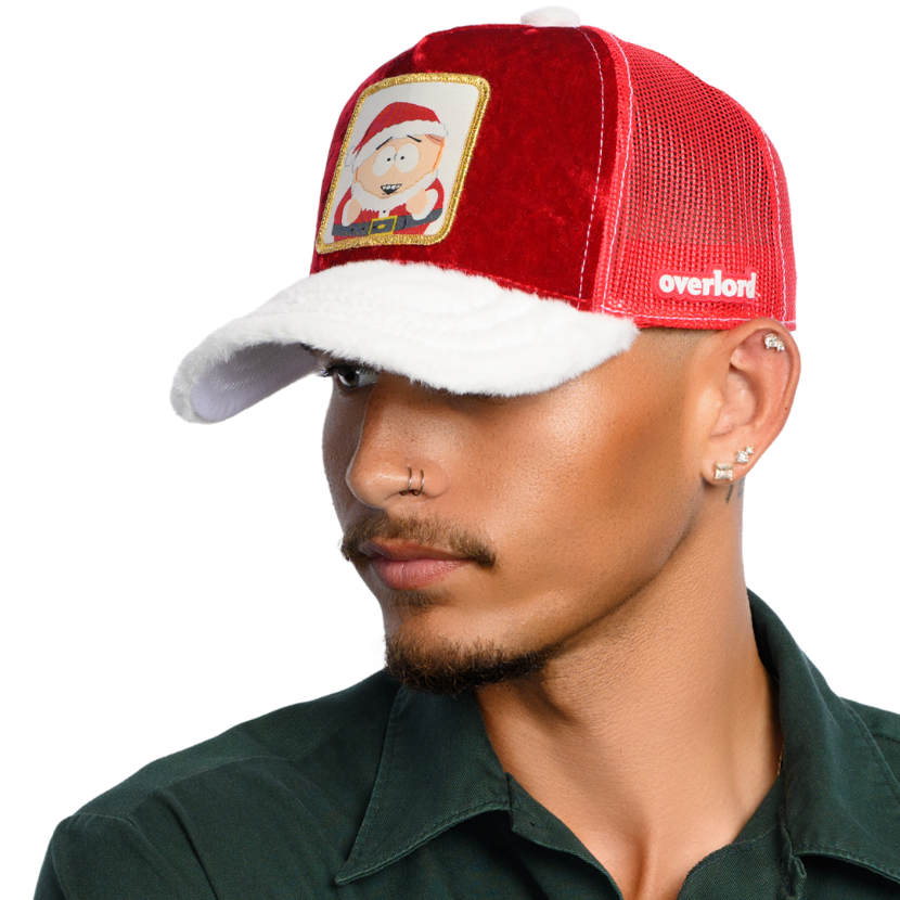 Man wearing red crushed velvet trucker cap with white faux fur brim and red mesh featuring a woven patch of Cartman from South Park wearing a Santa suit attached to the crown.