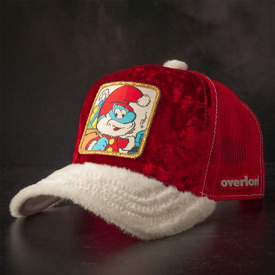Red crushed velvet trucker cap with white faux fur brim and red mesh featuring a woven patch of Papa Smurf from the Smurfs wearing a Santa suit and carrying a sack of presents attached to the crown.