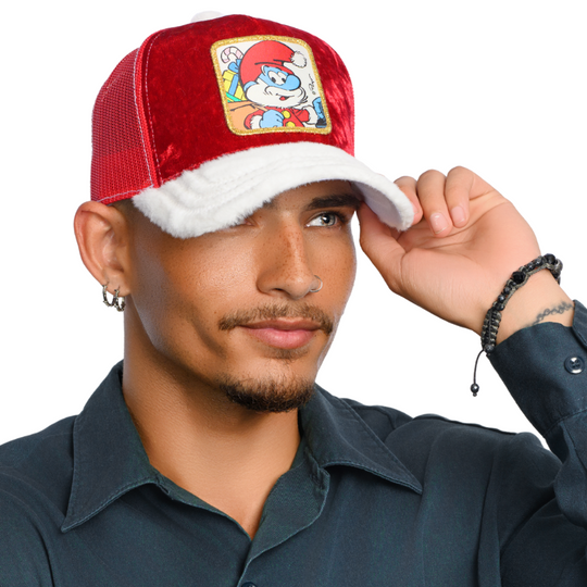 Man wearing red crushed velvet trucker cap with white faux fur brim and red mesh featuring a woven patch of Papa Smurf from the Smurfs wearing a Santa suit and carrying a sack of presents attached to the crown.