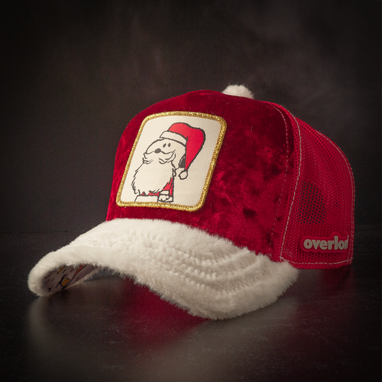 Red crushed velvet trucker cap with white faux fur brim and red mesh featuring a woven patch of Snoopy from the Peanuts wearing a Santa suit attached to the crown.